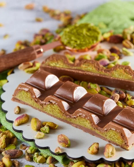 Barras recheadas DONUTRI com creme de pistache e cobertura de chocolate, cercadas por pistaches